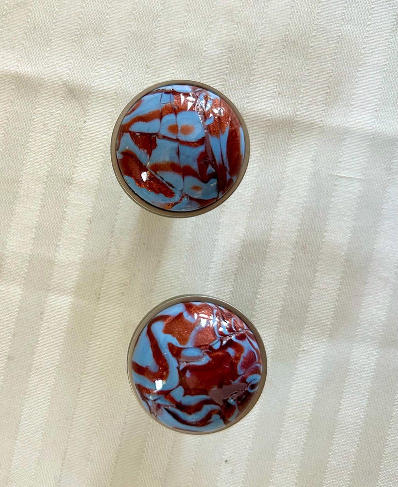 May include: Two round, blue and red marbled glass bottle stoppers. The stoppers have a shiny, iridescent finish.