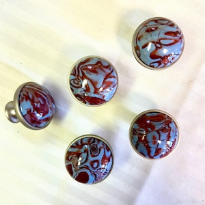May include: Five round, silver-toned cabinet knobs with blue and red marbled designs.