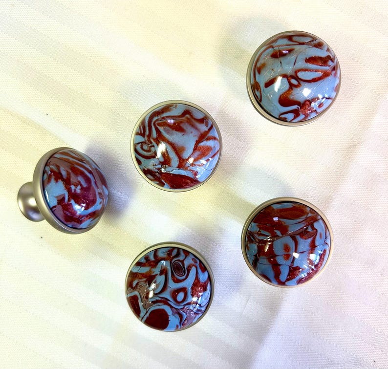 May include: Five round, silver-toned cabinet knobs with blue and red marbled designs.