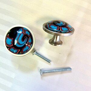 May include: Two decorative cabinet knobs with a black, white, red, and blue swirl design. The knobs have a silver base and come with two screws.