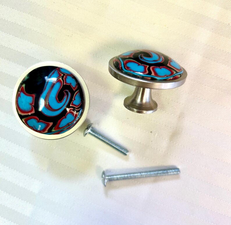 May include: Two decorative cabinet knobs with a black, white, red, and blue swirl design. The knobs have a silver base and come with two screws.