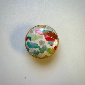 May include: A round wooden knob with a colourful abstract design. The design features shades of red, green, blue, and yellow.