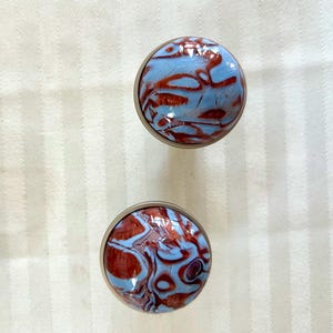 May include: Two round, silver-colored knobs with a blue and brown marbled design. The knobs have a smooth, shiny finish.