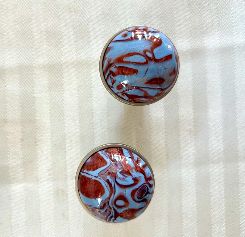 May include: Two round, silver-colored knobs with a blue and brown marbled design. The knobs have a smooth, shiny finish.