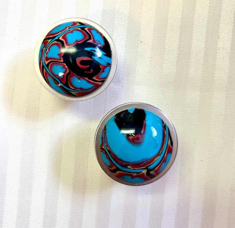 May include: Two round, silver-colored, decorative knobs with a blue, black, and red marbled design.
