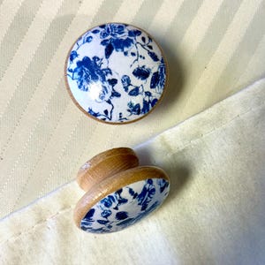 Può includere: Due pomelli in legno con un design floreale blu e bianco. I pomelli sono rotondi e hanno una superficie liscia.