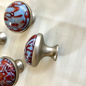 May include: Four cabinet knobs with a silver base and a blue and red marbled design.