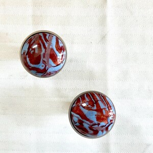 May include: Two round, silver-toned knobs with a blue and red marbled design.