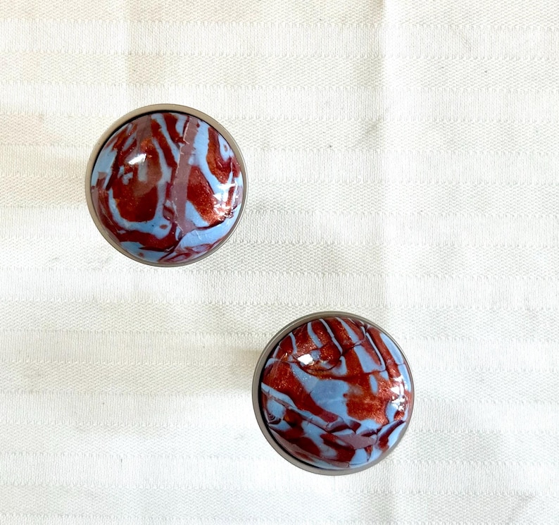 May include: Two round, silver-toned knobs with a blue and red marbled design.
