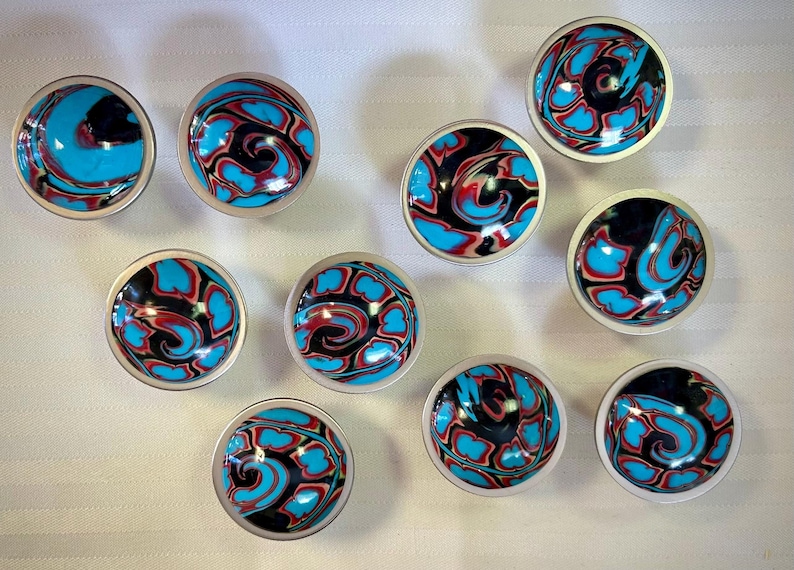 May include: Ten small, round, silver-rimmed bowls with a swirling pattern of black, blue, and red paint.