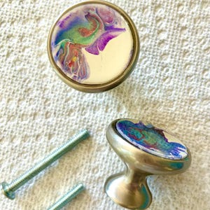 May include: Two silver cabinet knobs with round, white bases and colourful abstract designs. The knobs come with two silver screws.