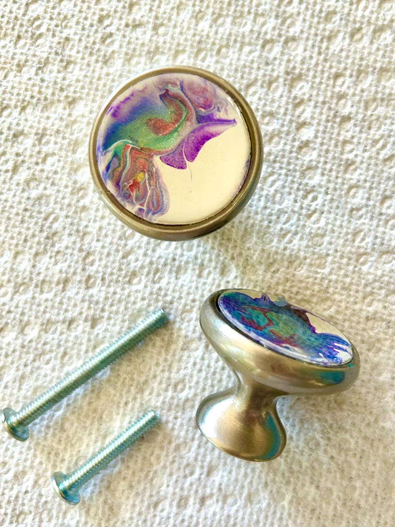 May include: Two silver cabinet knobs with round, white bases and colourful abstract designs. The knobs come with two silver screws.