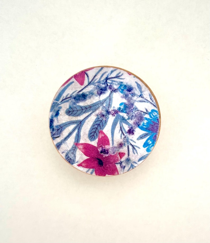 K&ouml;nnte beinhalten: Ein rundes Objekt mit floralem Muster und Holzrand. Das Design zeigt einen wei&szlig;en Hintergrund mit blauen, lila und pinkfarbenen Blumen und Bl&auml;ttern. Das Objekt ist vor einem wei&szlig;en Hintergrund zentriert.