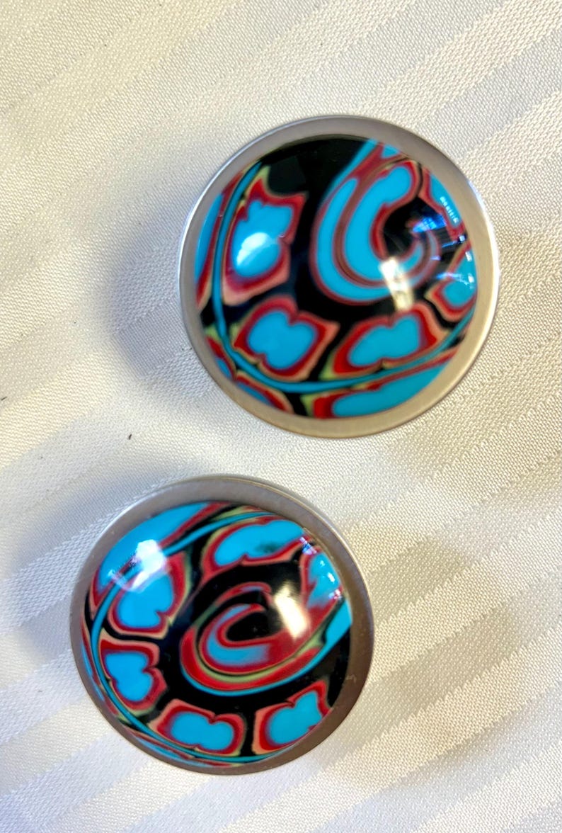 May include: A pair of round, silver-toned earrings with a black, blue, red, and green swirl pattern.