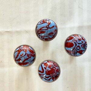 May include: Four round, blue and red marbled cabinet knobs. The knobs have a metallic finish.