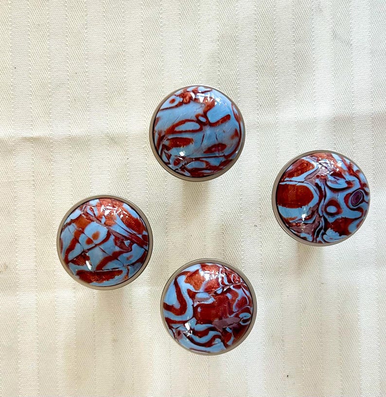 May include: Four round, blue and red marbled cabinet knobs. The knobs have a metallic finish.
