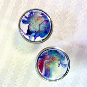 May include: Two round, silver-rimmed, white ceramic knobs with abstract blue, purple, and pink marbling.