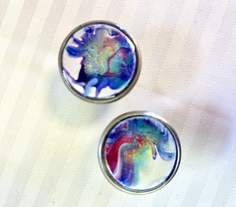 May include: Two round, silver-rimmed, white ceramic knobs with abstract blue, purple, and pink marbling.