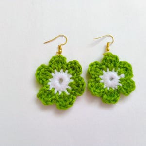 Op de afbeelding: Een paar gecrochete bloemoorbellen in groen en wit. De oorbellen zijn gemaakt met een wit centrum en groene bloemblaadjes.