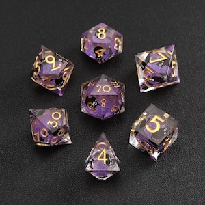 Peut inclure: Ensemble de sept dés polyédriques avec un design en résine violette et transparente. Les dés ont des chiffres dorés et des accents noirs. Idéal pour les jeux de rôle sur table.