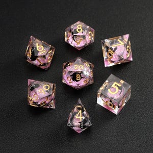 Op de afbeelding: Set van zeven heldere harsdobbelstenen met roze glitter en zwarte accenten. De cijfers zijn goudkleurig. De dobbelstenen zijn voor rollenspellen en bevatten een D4, D6, D8, D10, D12 en D20.