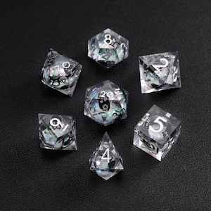 Könnte beinhalten: Ein Set aus sieben transparenten, vielseitigen Würfeln mit schillernden Einschlüssen und weißen Zahlen. Die Würfel sind auf einer dunklen Oberfläche angeordnet, wodurch ihre verschiedenen geometrischen Formen und nummerierten Flächen hervorgehoben werden. Für Tischspiele.