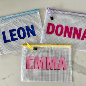 May include: Three clear mesh zippered pouches with different colored trim. The pouches have names printed on them: Leon, Donna, and Emma.