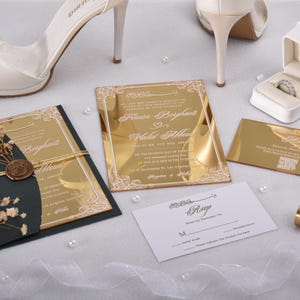 May include: Gold and black wedding invitations with a gold mirror finish. The invitations feature a white floral design and the text "Alice & Bayleigh" and "Wedding Album".