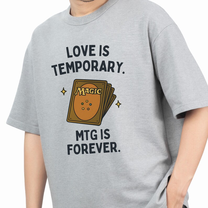 K&ouml;nnte beinhalten: Graues T-Shirt mit einem Grafikdruck einer Magic: The Gathering Karte und dem Text "Liebe ist verg&auml;nglich. MTG ist f&uuml;r immer."