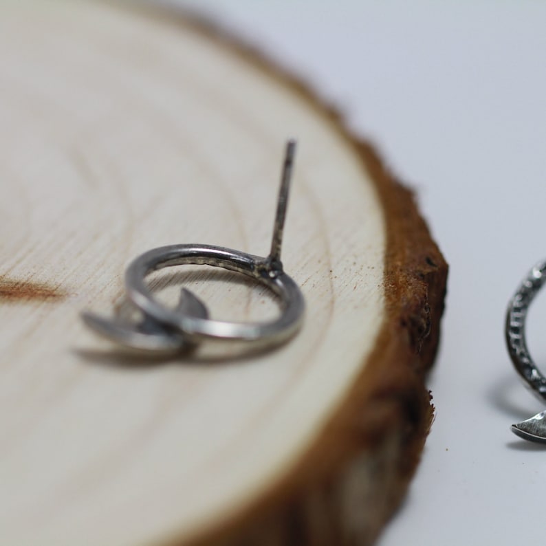 Op de afbeelding: Een paar zilveren halve maan oorbellen met een steek sluiting. De oorbellen liggen op een houten oppervlak.