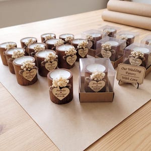 May include: A collection of cylindrical wooden candle holders, each containing a white tea light candle. A small heart-shaped wooden tag is attached to the front, engraved with "James & Kristal 8.22.26" and topped with dried white flowers.