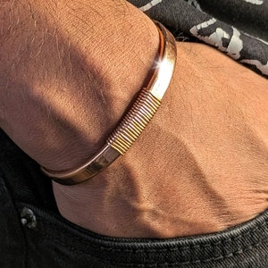 May include: A gold-toned metal bracelet with a textured design. The bracelet is worn on a person's wrist.