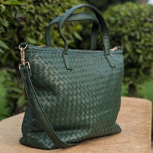 May include: A dark green woven leather tote bag with a top zipper closure and a long adjustable shoulder strap.