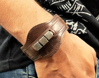 May include: A brown leather cuff bracelet with a silver metal accent. The metal accent is made up of four rectangular pieces.