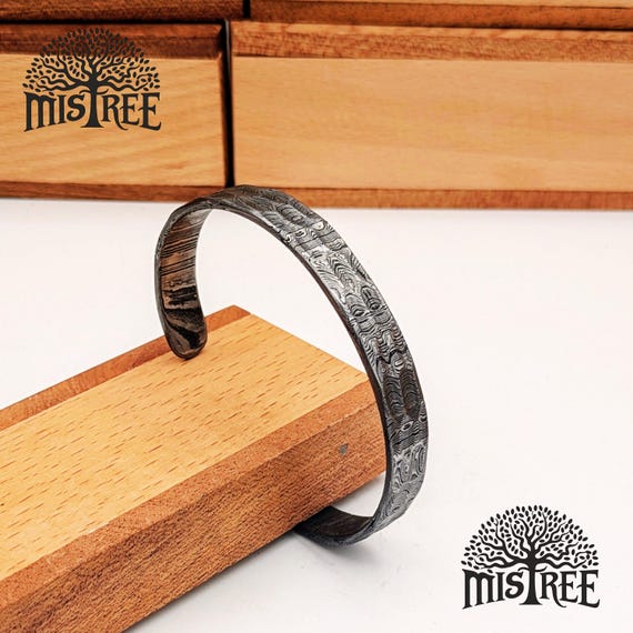 Hand-forged Damascus steel with visible layered pattern and Viking filework — a bracelet a blacksmith actually hammered into shape, not cast or printed.