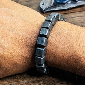 Puede incluir: Un brazalete plateado hecho de eslabones metálicos cuadrados. El brazalete está hecho de un metal estampado, lo que le da un aspecto único.