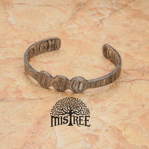 May include: A silver bracelet with a patterned design and a series of rounded shapes. The bracelet is on a light brown marble surface. The logo "Mistree" is visible below the bracelet.