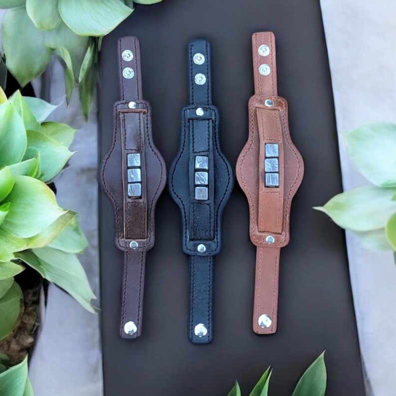 May include: Three leather bracelets with silver metal accents. The bracelets are brown, black, and tan.