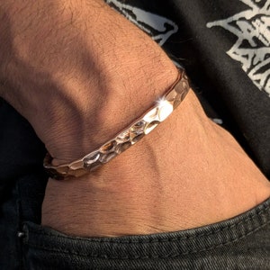 Peut inclure: Un bracelet en cuivre martelé avec une finition texturée. Le bracelet est porté au poignet.