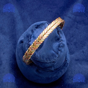 May include: A gold, copper and silver bracelet with a chevron pattern. The bracelet is made of three different metals, each with a different colour.