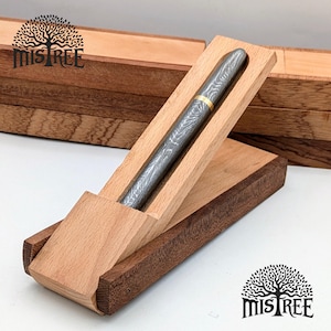 May include: A silver pen with a patterned design and gold band rests in an open wooden pen case. The case is made of light and dark brown wood. The pen case is angled, and the pen is visible. The brand name "MISTREE" is visible.