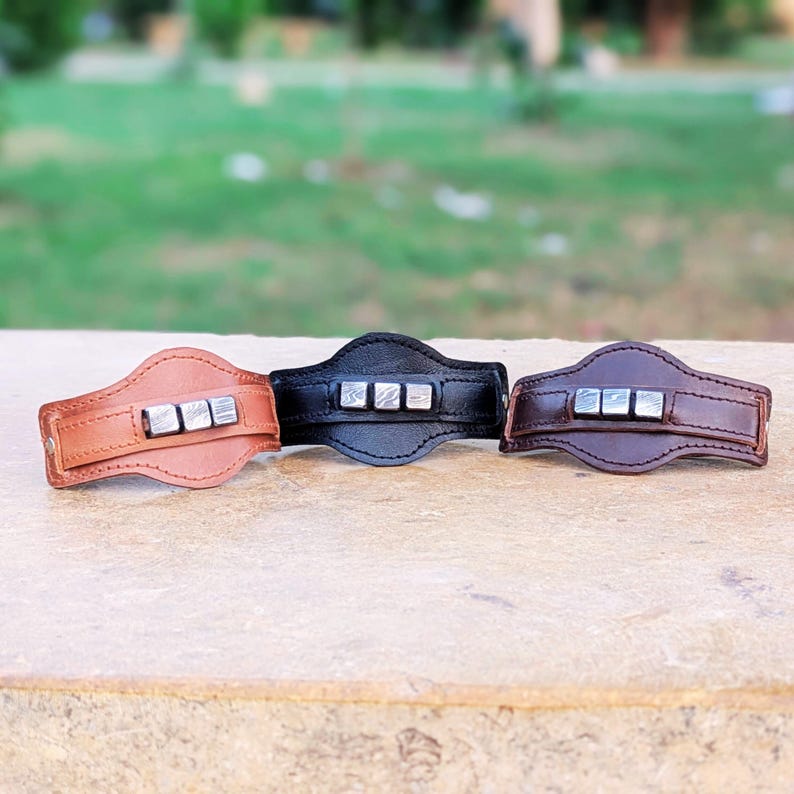 May include: Three leather bracelets with silver metal accents. The bracelets are brown, black, and dark brown.