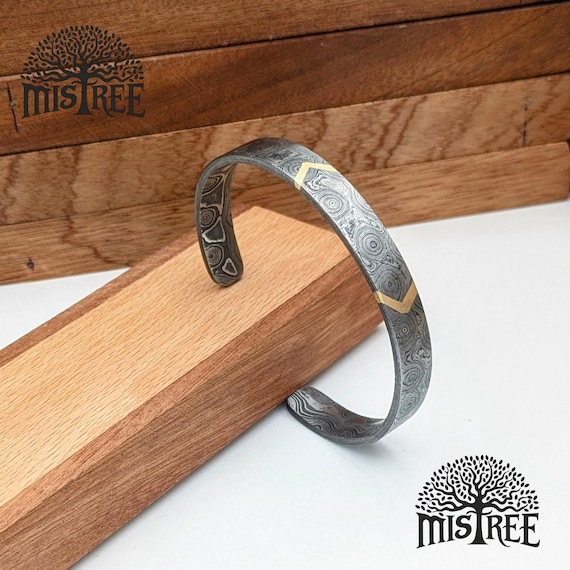Hand-forged Damascus steel with a brass arrow inlay — the swirling pattern of real pattern-welded steel makes every bracelet genuinely one-of-a-kind, and the Norse aesthetic elevates it way beyond generic men's jewelry.