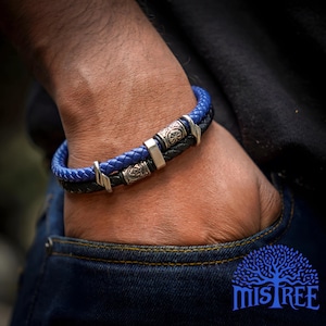 May include: A black and blue leather bracelet with silver metal accents. The bracelet has a braided design and features decorative metal beads.