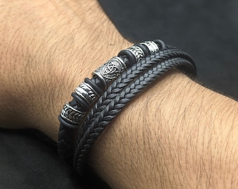 May include: A black leather bracelet with silver metal beads featuring a Celtic knot design.