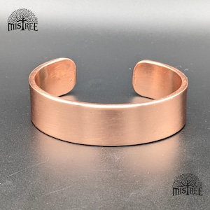 May include: A copper cuff bracelet with a smooth, brushed finish. The open-ended design allows for easy wear. The bracelet has a width of approximately 0.5 inches.