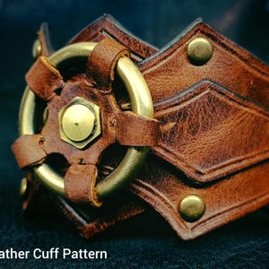 May include: Brown leather cuff with brass accents. The cuff features a geometric design with rivets and a central brass ring. The text "Leather Cuff Pattern" is visible at the bottom of the image.