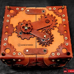 May include: A square, steampunk-style leather box with a hinged lid. The box features a light brown interior and dark brown exterior with gear-shaped accents, rivets, and a gear mechanism on the front. The box has the text "LEATHER PATTERNIQUE".