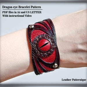 Könnte beinhalten: Ein handgefertigtes Lederarmband mit einem Drachenaugen-Design. Das Armband ist hauptsächlich rot und braun, mit einem zentralen roten Auge und strukturierten Details. Der Text "Dragon eye Bracelet Pattern" ist sichtbar.