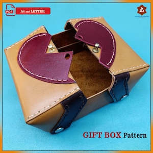 May include: A tan leather gift box with a burgundy heart-shaped lid. The box is open and the inside is visible. The box is made of leather and has a brown leather trim. The box is labelled "GIFT BOX Pattern".